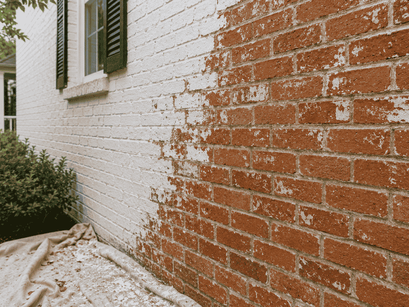 Partially restored painted brick exterior showing white paint being removed to reveal the original red brick on a home in McKinney, TX.