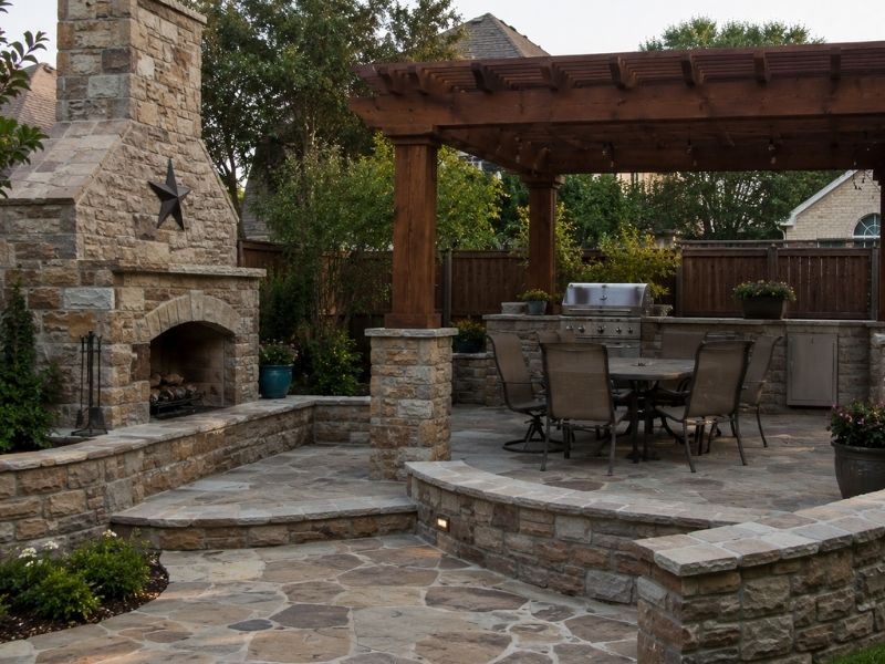 Realistic custom backyard with natural stone patio, fireplace, seating walls, and outdoor kitchen features in McKinney, TX.