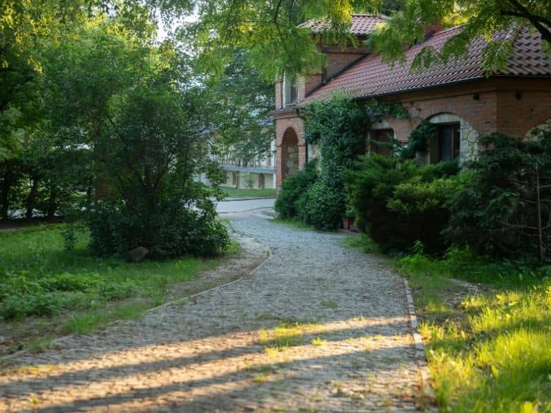 Landscaped residential yard with mature greenery surrounding a brick and stone home and walkway